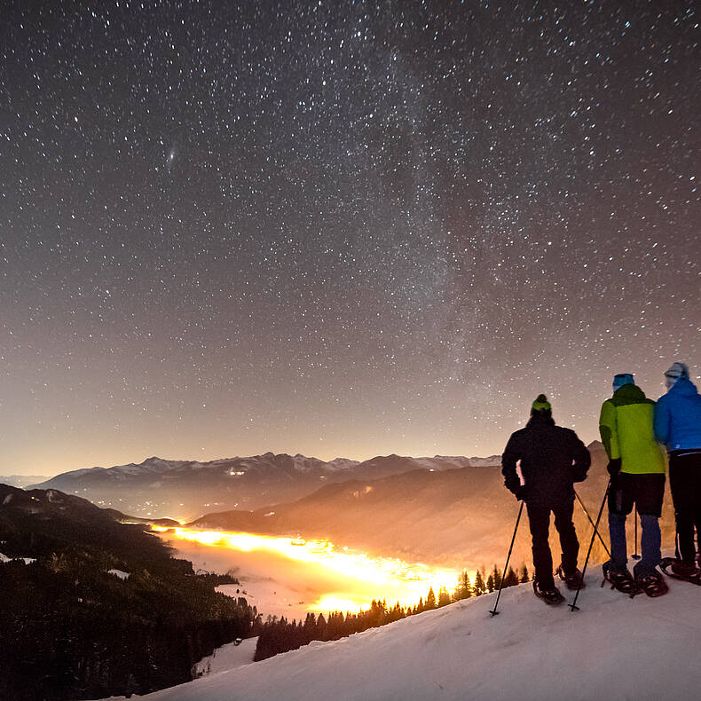 Winterwanderer genießen den Sternenhimmel über dem Weissensee in verschneiter Wintelandschaft.